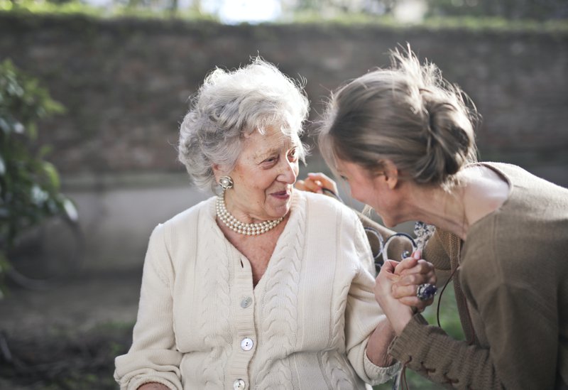 an elderly woman sitting outside smiling with her caregiver