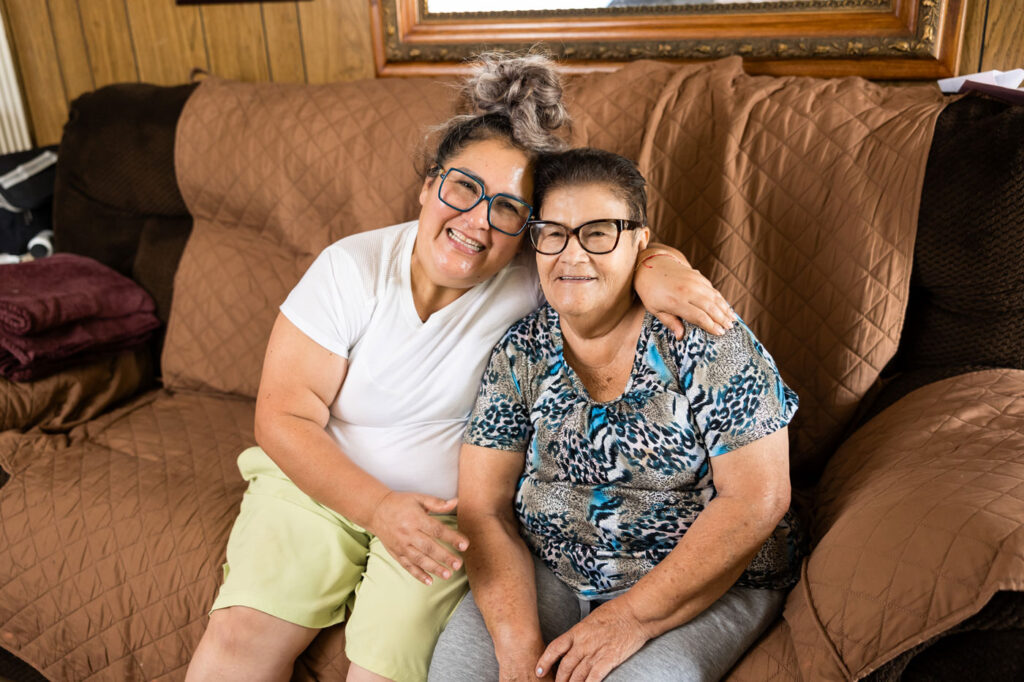 an elderly woman and her caregiver sitting on the couch and smiling together
