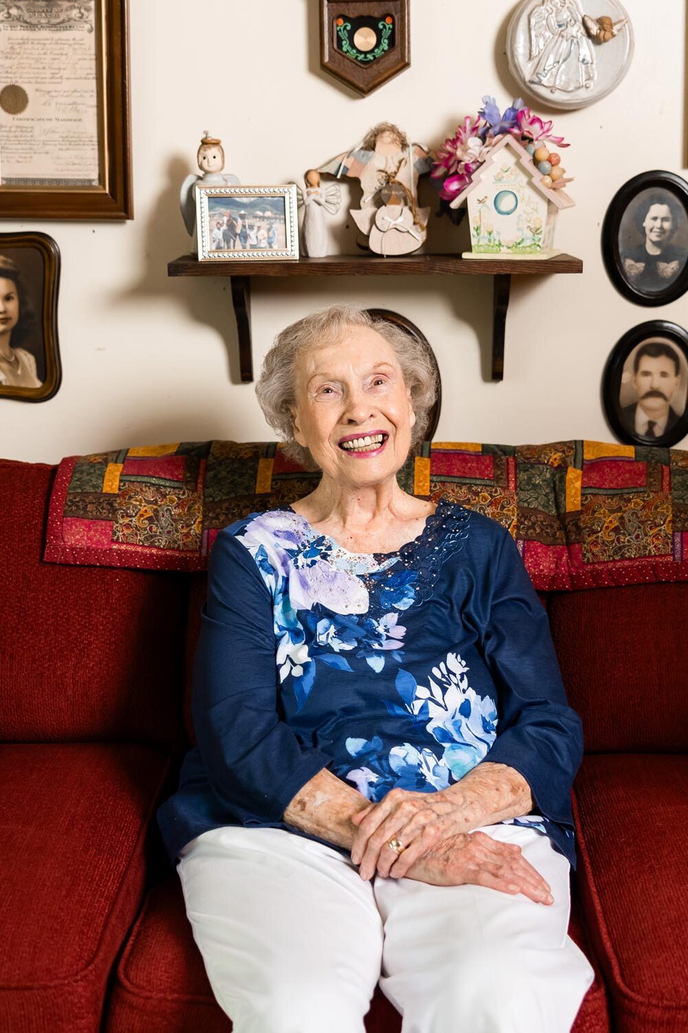 Jean sitting on her red couch in front of all her photos