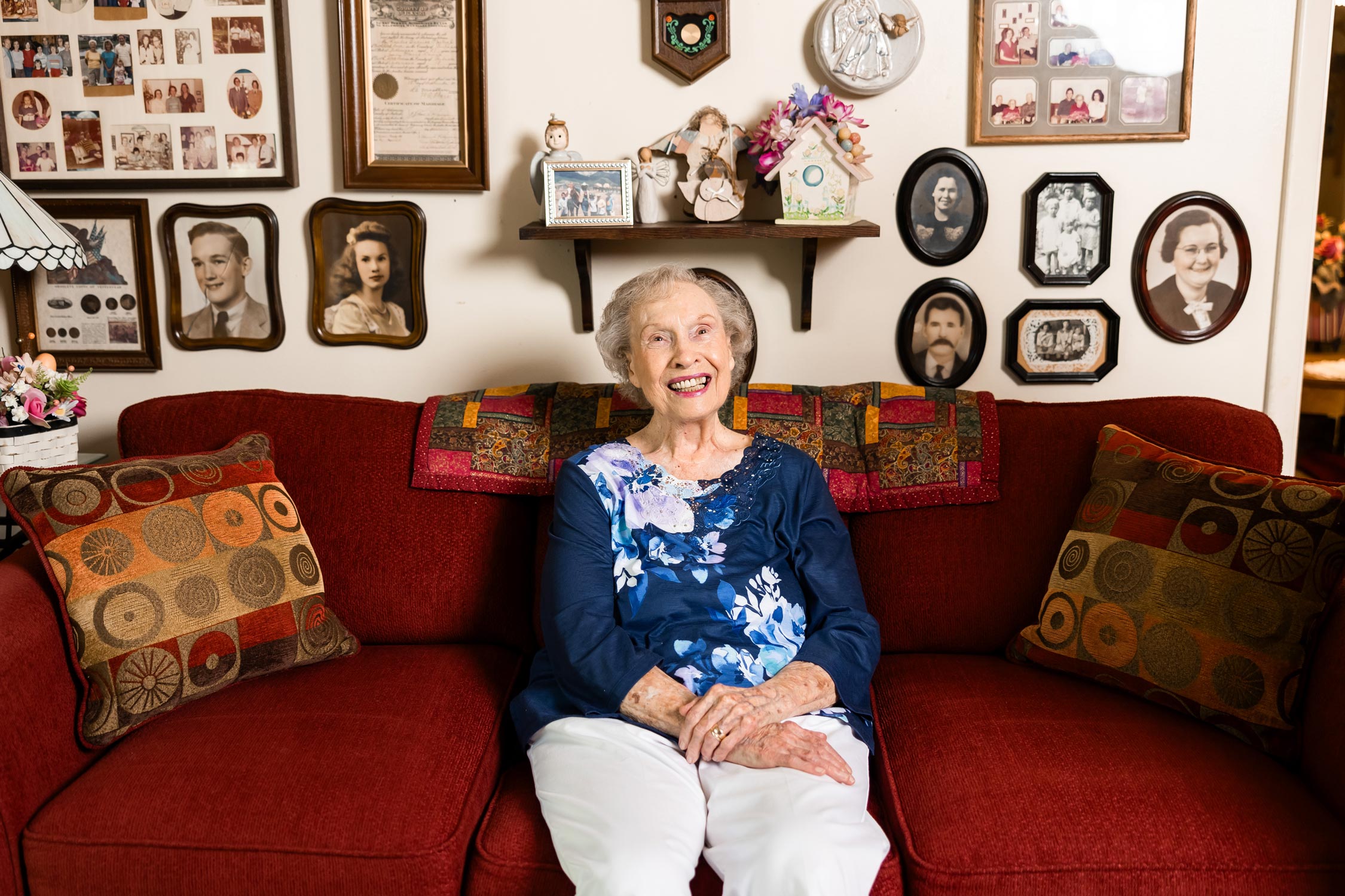 Jean sitting on her red couch in front of all her photos
